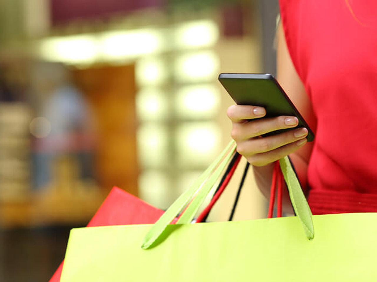 Frau mit Einkaufstaschen und einem Mobiltelefon in der rechten Hand